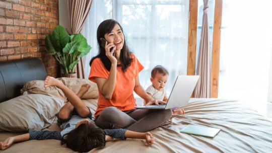 young woman working on her bed while taking care of her unruly children at home