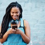 Black woman with 5g smartphone for social media typing, digital chat app or check location on blue wall background space mockup. Teenager gen z girl on cellphone for youth online website networking