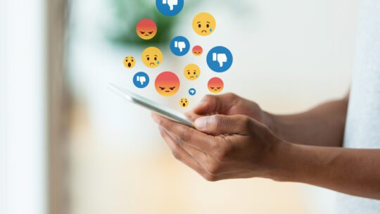 person holding a tactile mobile smartphone sending text messages with negative emojis to symbolize an influencer crisis