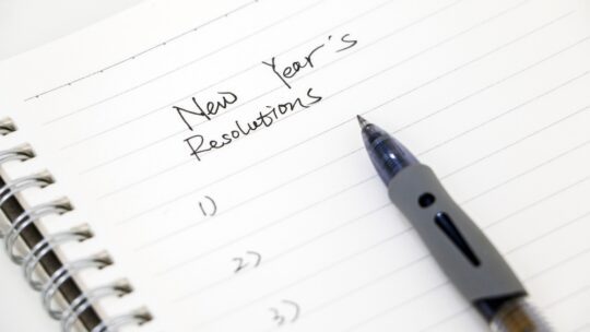 Writing new year’s resolutions, list on white notepad with ballpoint pen. Setting goals for the new year.