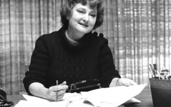 An image of Betsy Plank working at her desk with a pile of papers