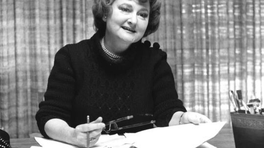 An image of Betsy Plank working at her desk with a pile of papers