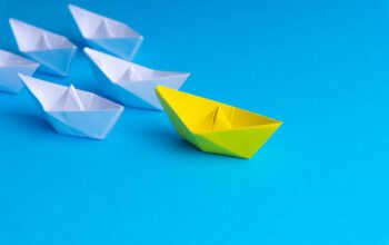 White and yellow paper boat or ship in one direction on blue background, representative of a thought leader engaging the community.