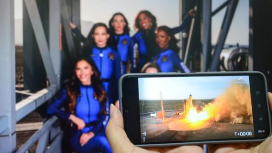 People use smartphone with an image of a spacecraft launch to watch news about Katy Perry and others successfully flying into space and returning to Earth aboard the Blue Origin spacecraft.
