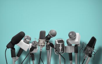 Press conference with standing microphones on an aqua blue background