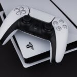 A white Sony Playstation 5 controller and PlayStation 5 console on a dark table. Sony said the console will now have a power saving option.