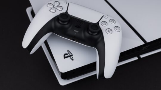 A white Sony Playstation 5 controller and PlayStation 5 console on a dark table. Sony said the console will now have a power saving option.