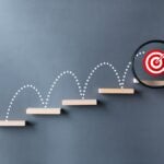 Unlock potential of business success stairs dart and dartboard targets magnifying glass with hand on gray background. Explore opportunities growth embrace steps to achieve ambitions and goal concept.