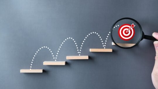 Unlock potential of business success stairs dart and dartboard targets magnifying glass with hand on gray background. Explore opportunities growth embrace steps to achieve ambitions and goal concept.