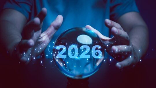 A glowing crystal ball with the year 2026 illuminated inside surrounded by human hands and digital sparkles. This image symbolizes prediction, foresight, planning, and vision for the future.