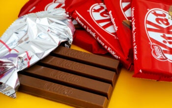 One open KitKat chocolate bar surrounded by other kitkat bars on a yellow background.