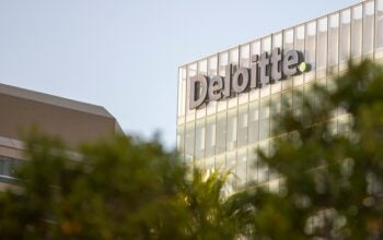 This image features the top of the Deloitte building, with the company's name prominently displayed in large letters on the glass facade.
