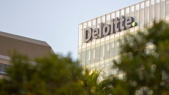 This image features the top of the Deloitte building, with the company's name prominently displayed in large letters on the glass facade.
