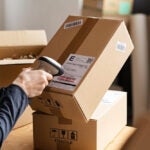 Hands scanning barcode on delivery parcel. Worker scan barcode of cardboard packages before delivery at storage. Woman working in factory warehouse scanning labels on the boxes with barcode scanner.