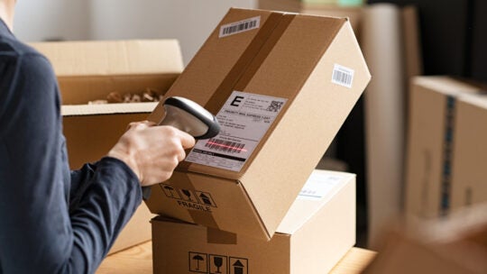 Hands scanning barcode on delivery parcel. Worker scan barcode of cardboard packages before delivery at storage. Woman working in factory warehouse scanning labels on the boxes with barcode scanner.
