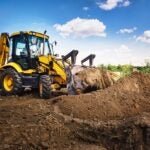 Excavator working at house construction site - digging foundations for modern house. Beginning of house building. Earth moving and foundation preparation.