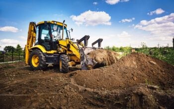 Excavator working at house construction site - digging foundations for modern house. Beginning of house building. Earth moving and foundation preparation.