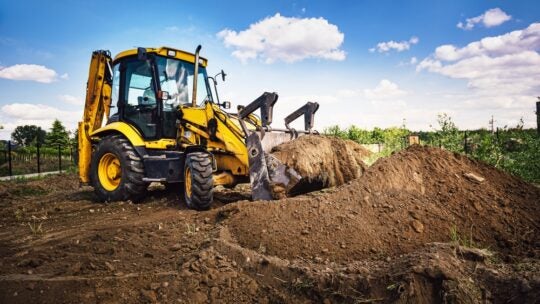 Excavator working at house construction site - digging foundations for modern house. Beginning of house building. Earth moving and foundation preparation.