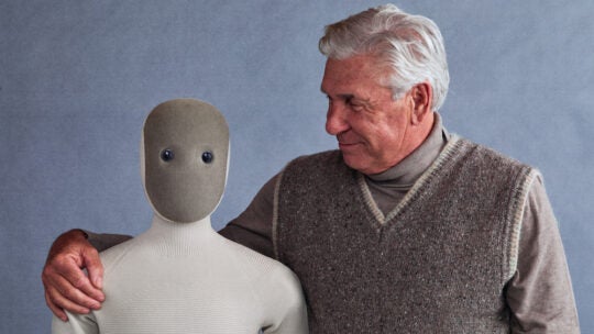 elderly man squeezing the Neo robot around his shoulders like a hug. this relates to the product mentioned in this bad coverage article.