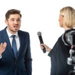 journalist interviewing angry businessman near camera