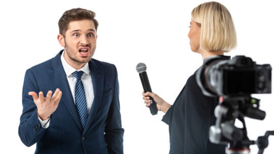 journalist interviewing angry businessman near camera