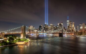 Elevated view of September 11 Tribute in Light. Twin beams of light and skyscrapers of Lower Manhattan. Financial District with Brooklyn Bridge, and East River
