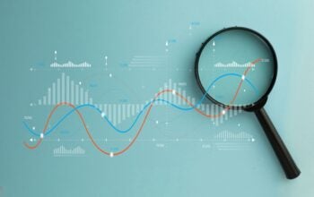 Magnifying glass over digital data graph and charts. Business analytics, financial market research, and statistics concept. Stock market, investment, and data audit.